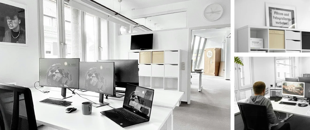 Arbeitsplatz mit drei Monitoren und Laptop im Großraumbüro, Schild „Filmen und Fotografieren verboten!“, Mitarbeiter am Schreibtisch